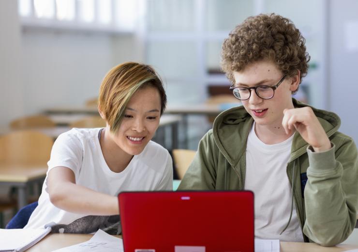 Två ungdomar sitter bredvid varandra och tittar in i en röd laptop